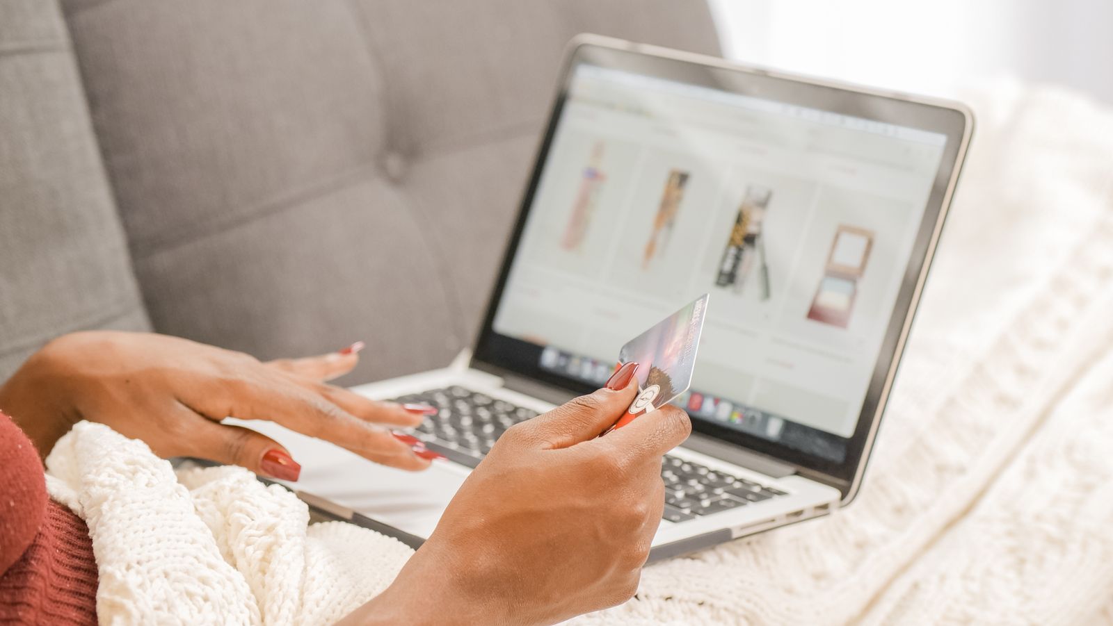 Una persona compra online desde el sofa con el portatil y una tarjeta en la mano.