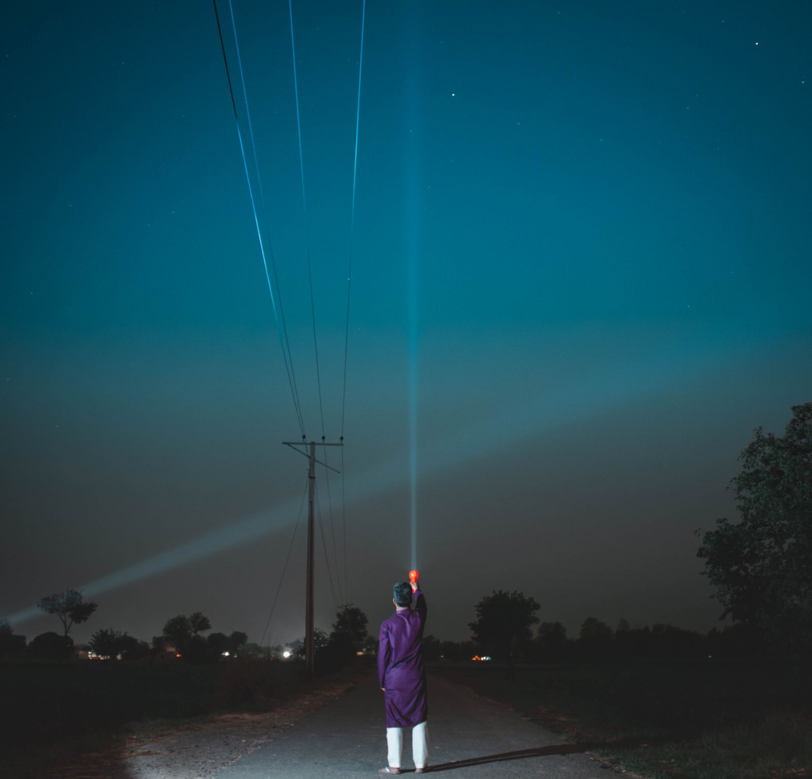 Un hombre ilumina la noche con una linterna en un camino rural.